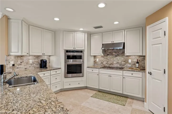 Kitchen featuring white cabinets, double oven, light stone counters, recessed lighting, and under cabinet range hood