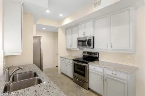 Kitchen featuring a sink, visible vents, light stone countertops, and appliances with stainless steel finishes