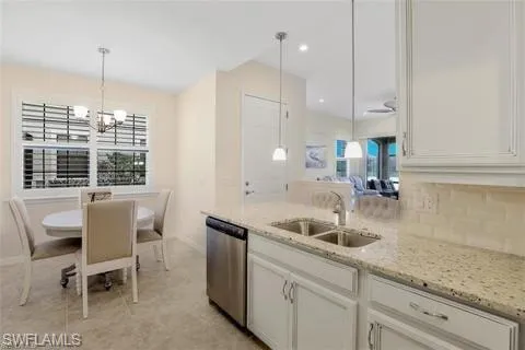 Kitchen featuring white cabinetry, a sink, stainless steel dishwasher, and light stone counters