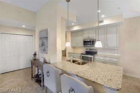 Kitchen featuring a peninsula, light stone countertops, stainless steel appliances, a sink, and a breakfast bar area