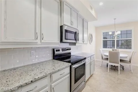 Kitchen featuring a chandelier, decorative backsplash, light stone counters, visible vents, and appliances with stainless steel finishes