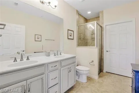 Full bathroom with visible vents, double vanity, toilet, a sink, and a stall shower