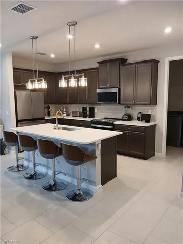 Kitchen featuring a breakfast bar area, dark wood finish cabinetry, stainless steel appliances, a kitchen island with sink, and hanging light fixtures