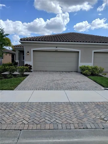 View of front facade featuring decorative driveway, a tiled roof, a garage, and stucco siding