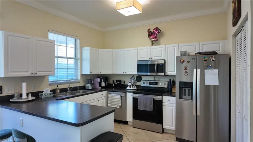Kitchen with stainless steel appliances, dark countertops, white cabinets, a peninsula, and crown molding