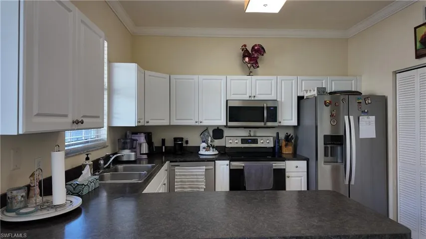 Kitchen with dark countertops, stainless steel appliances, white cabinets, ornamental molding, and a peninsula