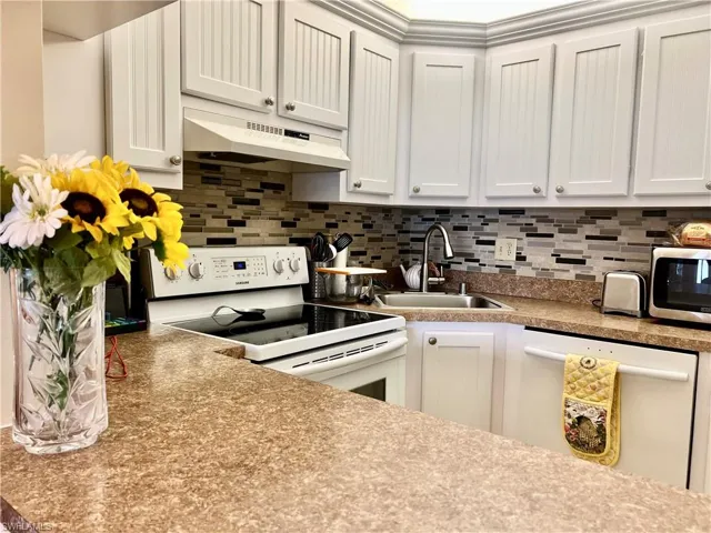 Kitchen with white appliances, light countertops, tasteful backsplash, and white cabinetry