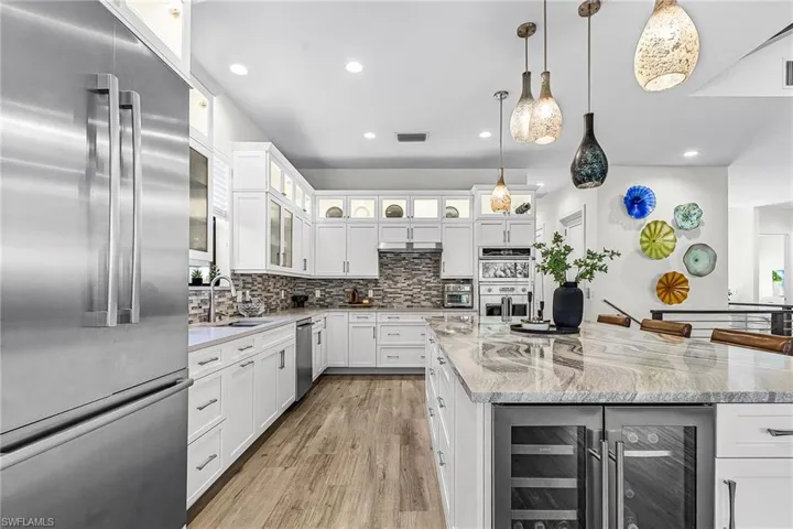 Kitchen featuring stainless steel appliances, white cabinets, beverage cooler, light stone countertops, and recessed lighting