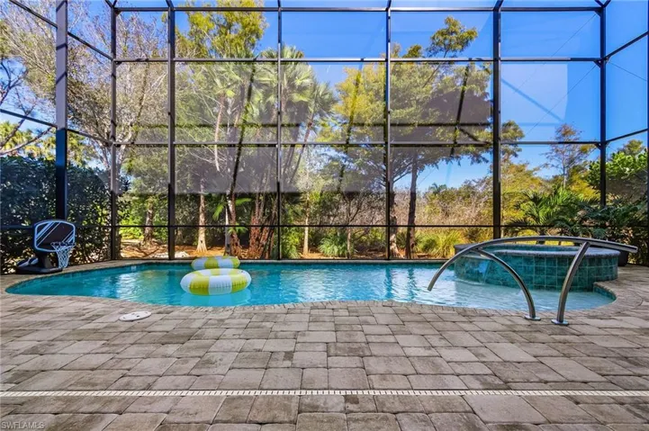 View of pool featuring glass enclosure, a pool with connected hot tub, and a patio