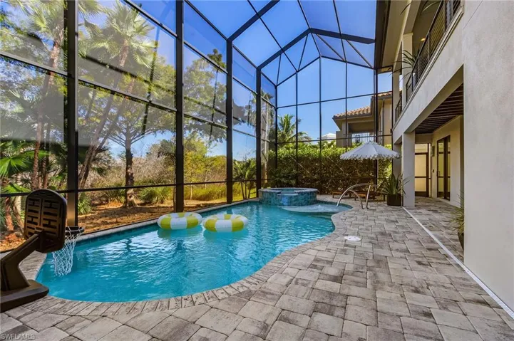 View of pool featuring glass enclosure, a patio, a sunroom, and a pool with connected hot tub
