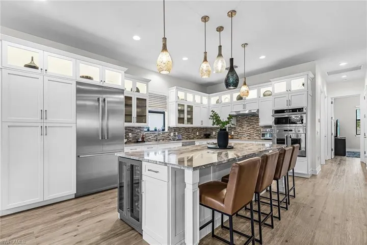 Kitchen featuring light stone counters, white cabinetry, appliances with stainless steel finishes, a kitchen breakfast bar, and backsplash