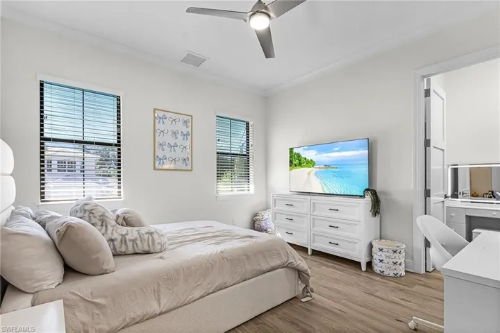 Bedroom with ornamental molding, connected bathroom, light wood finished floors, and ceiling fan