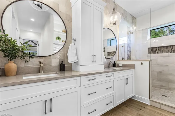 Bathroom with double vanity, a walk in shower, light wood finished floors, and tasteful backsplash