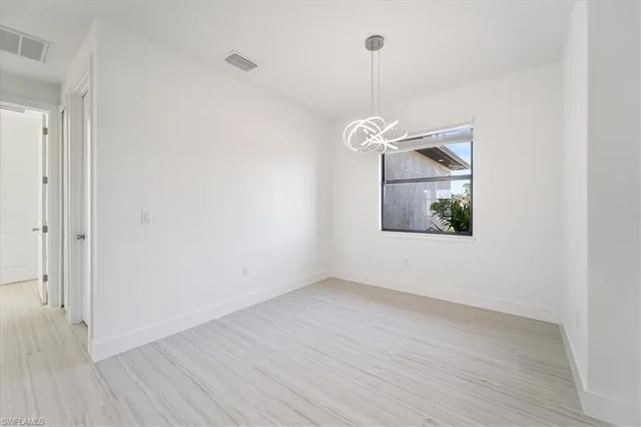 Spare room featuring light wood finished floors, baseboards, visible vents, and a chandelier