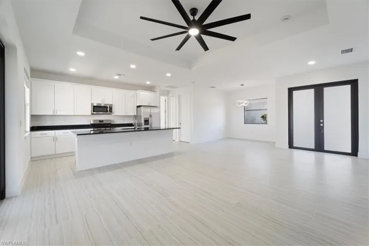 Kitchen featuring open floor plan, stainless steel appliances, a raised ceiling, dark countertops, and visible vents