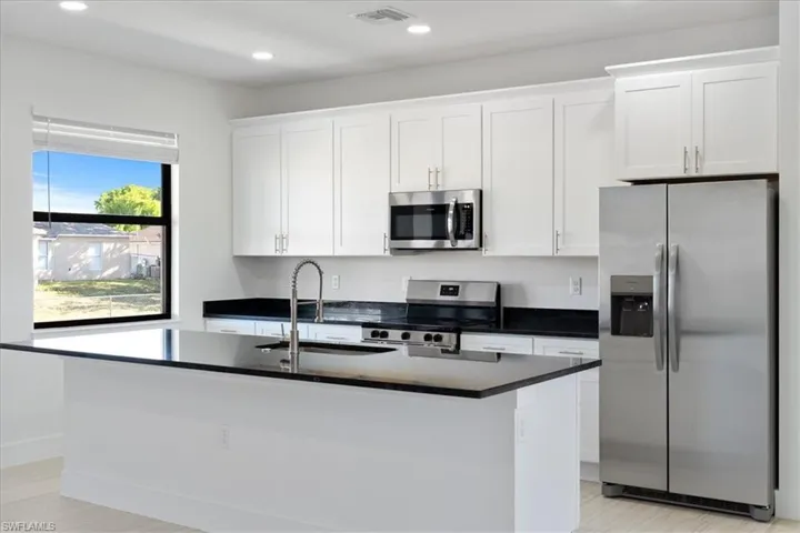Kitchen featuring white cabinetry, stainless steel appliances, a center island with sink, a sink, and visible vents