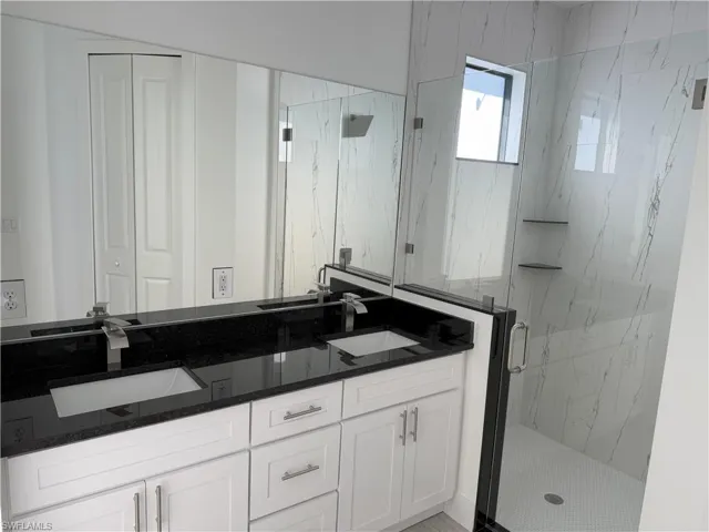 Bathroom featuring double vanity, a sink, and a marble finish shower