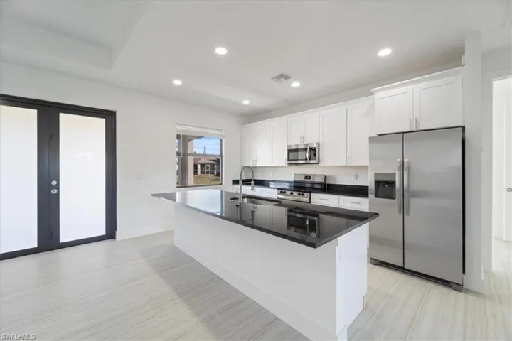 Kitchen with appliances with stainless steel finishes, white cabinetry, an island with sink, a sink, and french doors