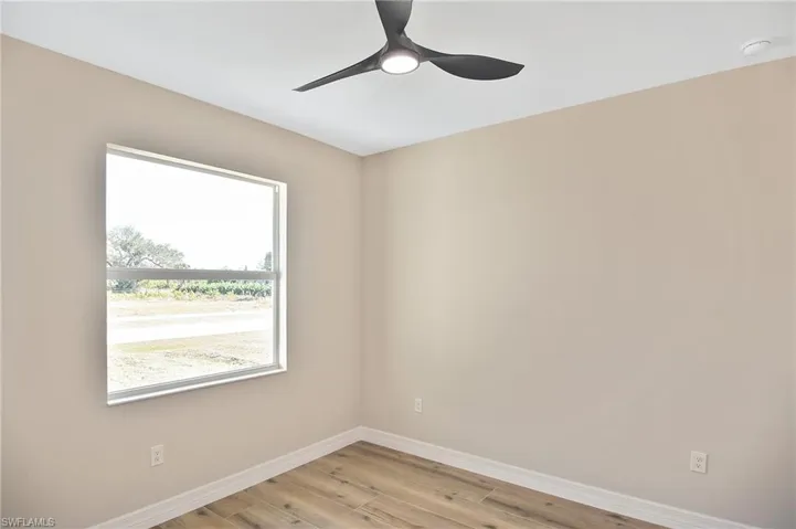 Bright interior space featuring a modern ceiling fan with integrated lighting, a large window, light neutral wall paint, white baseboards, and wood-finish flooring