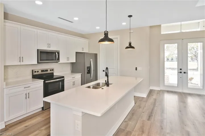 Kitchen featuring white shaker cabinetry, stainless steel appliances, and a central island with an undermount sink and two pendant lights