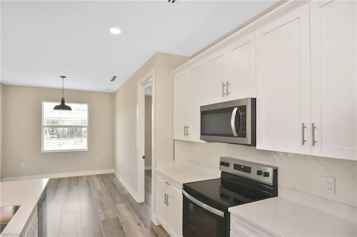 Contemporary kitchen featuring white shaker cabinetry, stainless steel appliances, light-toned countertops, and a subtle geometric pattern backsplash