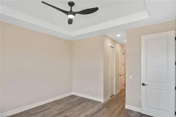 Tray ceiling with a modern ceiling fan, wood-finish flooring, recessed lighting, and white interior doors with black hardware
