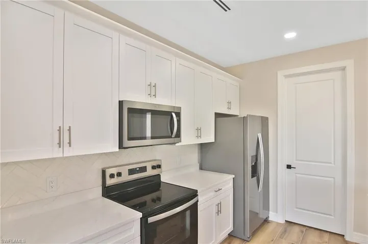 Kitchen featuring white shaker cabinetry, stainless steel appliances, light-toned countertops, a herringbone tile backsplash, and wood-finish flooring
