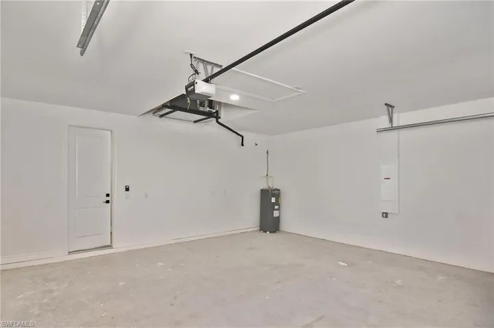 Spacious garage with concrete flooring, white painted walls, overhead garage door track system, and built-in water heater