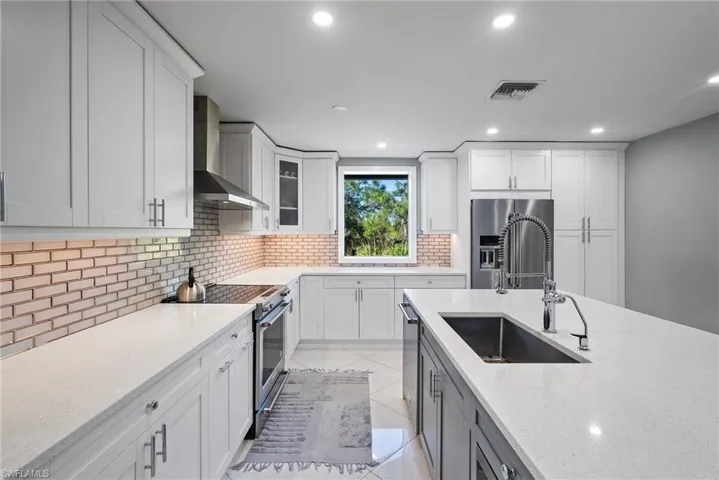 Kitchen with light stone counters, wall chimney exhaust hood, stainless steel appliances, sink, and white cabinetry