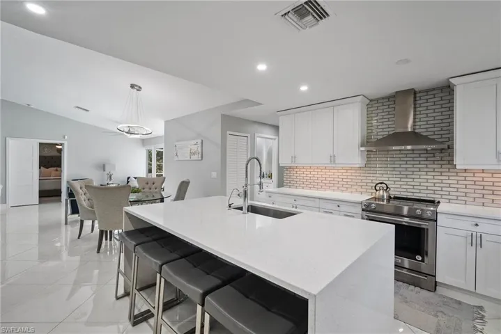 Kitchen featuring a center island with sink, wall chimney exhaust hood, stainless steel electric range oven, and sink