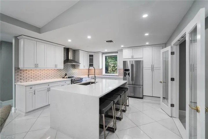 Kitchen with a kitchen island with sink, wall chimney range hood, sink, white cabinetry, and stainless steel appliances