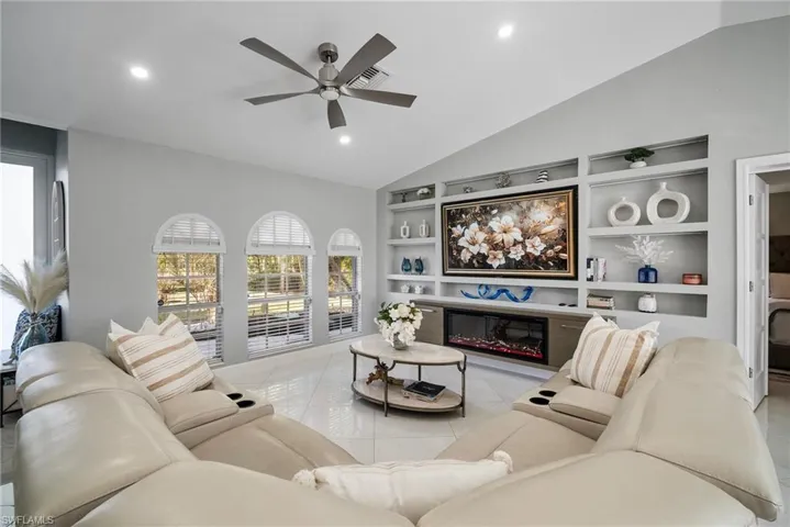 Tiled living room featuring built in shelves, ceiling fan, and vaulted ceiling