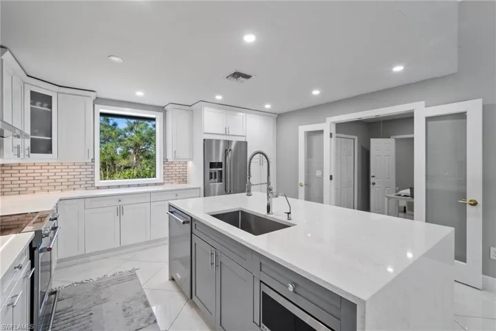 Kitchen featuring high end appliances, white cabinetry, sink, and a kitchen island with sink