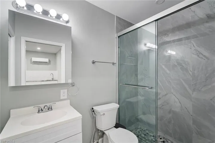 Bathroom with an AC wall unit, vanity, an enclosed shower, and toilet