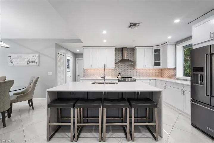 Kitchen featuring a kitchen island with sink, sink, wall chimney exhaust hood, white cabinetry, and stainless steel appliances