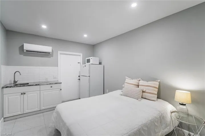 Bedroom with white fridge, sink, and a wall mounted AC