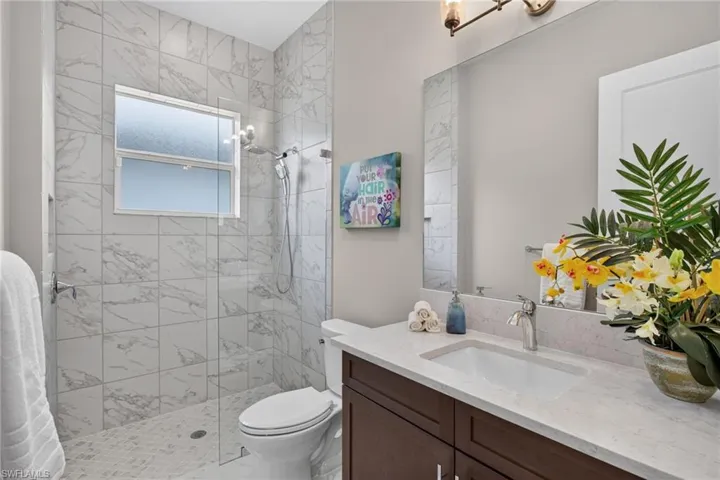 Spacious bathroom featuring a glass-enclosed shower with marble-look tile, a built-in window, and pebble-style flooring