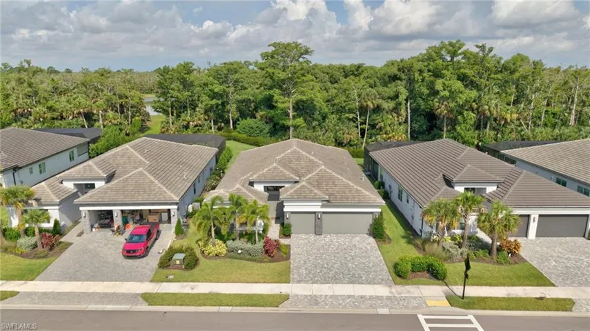 Modern dwelling with a tile roof and light-toned exterior, featuring a paver driveway, an attached garage, and manicured landscaping