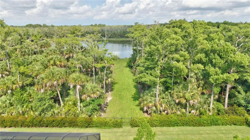Landscaped lawn leading to a private lake access path, bordered by mature trees and lush natural foliage
