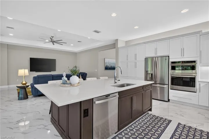 Open-concept kitchen featuring a large central island with integrated sink and dishwasher, white countertops, and stainless steel appliances
