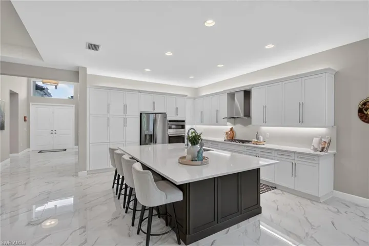 Gourmet kitchen featuring a large central island with a solid surface countertop, extensive white cabinetry, stainless steel appliances, and large format marble-look tile flooring