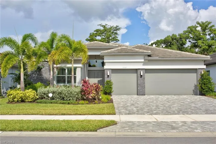 Contemporary stucco exterior with a tiled roof, paver driveway, two-car garage, and established landscaping featuring palm trees