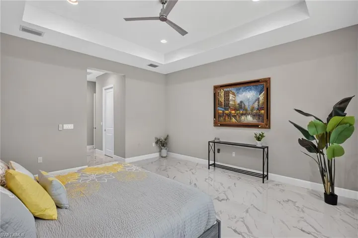 Spacious room featuring tray ceilings with recessed lighting, a ceiling fan, light gray wall tones, and large format marble-look tile flooring