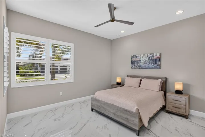 Spacious room featuring white plantation shutters, recessed ceiling lighting, a modern ceiling fan, and large format marble-look tile flooring
