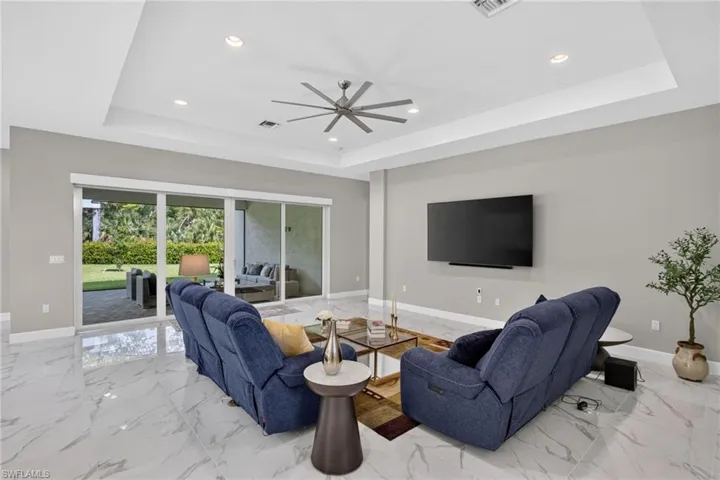 Spacious living area featuring large format white tile flooring, tray ceiling with recessed lighting, and expansive sliding glass doors opening to the exterior patio