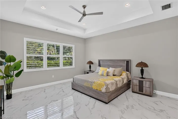 Spacious room featuring a tray ceiling with recessed lighting, a ceiling fan, and large windows with plantation shutters