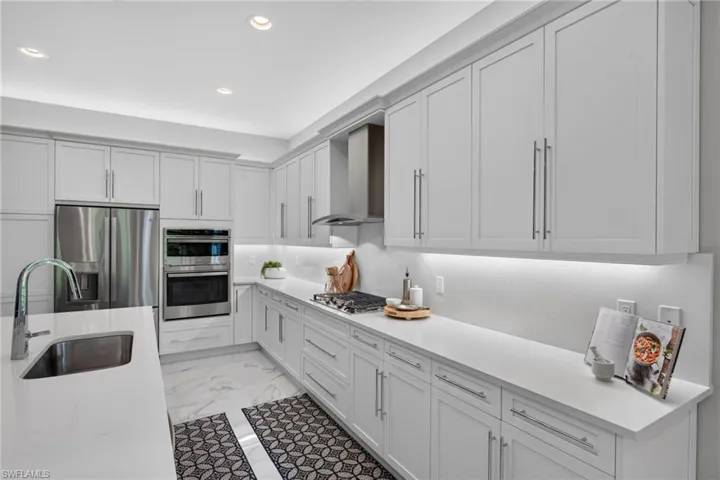 White shaker cabinetry with modern hardware, stainless steel appliances, marble-look tile flooring, undermount sink, and recessed lighting