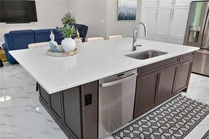 Kitchen island with a light-colored solid surface countertop, integrated stainless steel sink, and a chrome gooseneck faucet
