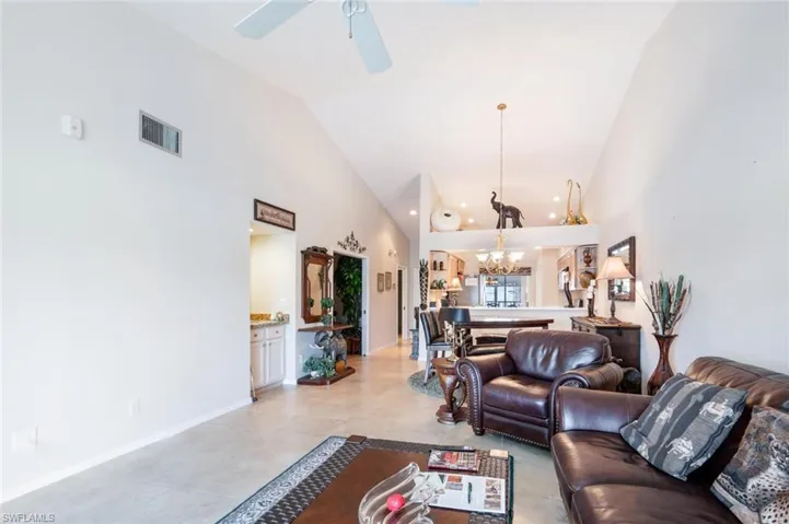 Living room featuring high vaulted ceiling, ceiling fan with notable chandelier, and light tile floors