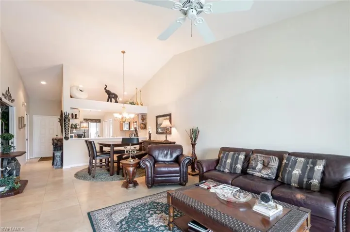 Tiled living room featuring high vaulted ceiling and ceiling fan with notable chandelier